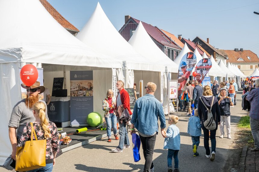 Volle Festmeile mit weißen Pagodenzelten, Familien schlendern an Ständen vorbei.