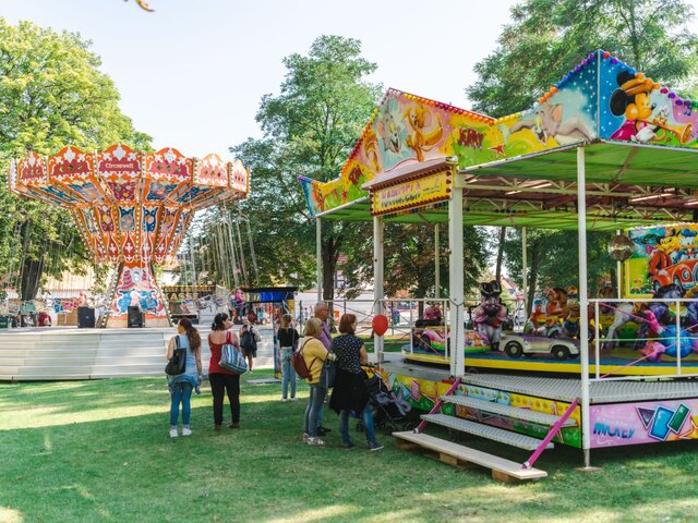 Kinderkarussell und Kettenkarussell auf einer Wiese unter alten Bäumen.