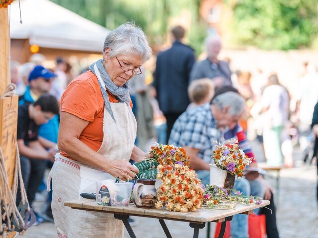 Eine Frau mit Schürze bindet Trockenblumen zu einem Kranz.
